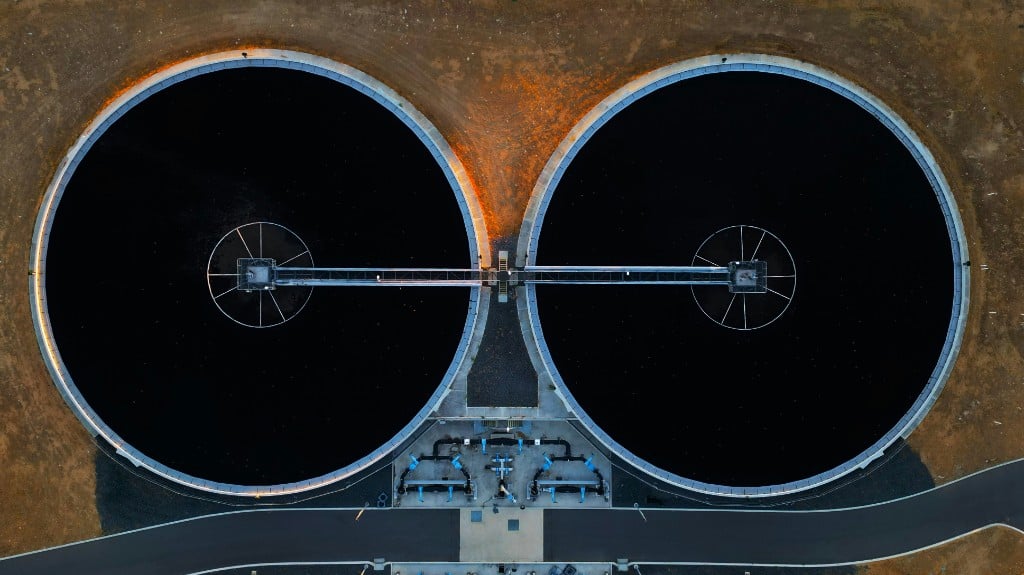 Bird's-eye view of two large circular clarification tanks with central walkways at an industrial water treatment facility.